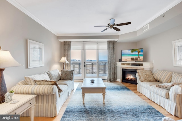 living area with visible vents, crown molding, ceiling fan, light wood-type flooring, and a lit fireplace