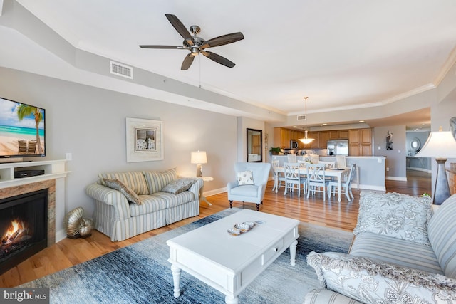 living room with visible vents, light wood-style floors, ornamental molding, and a fireplace