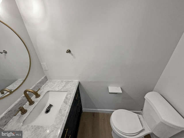 half bath with vanity, toilet, wood finished floors, and baseboards