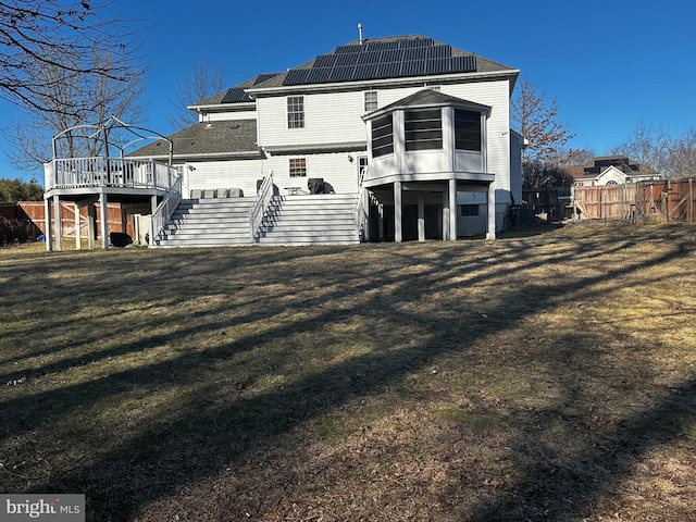 rear view of property featuring roof mounted solar panels, fence, a yard, a wooden deck, and stairs