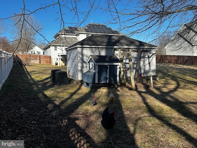 rear view of property with solar panels, an outdoor structure, a fenced backyard, and a lawn