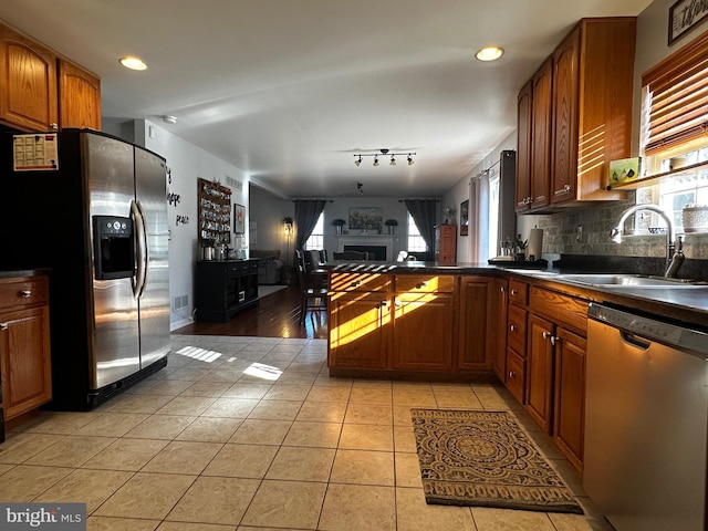 kitchen featuring a sink, dark countertops, stainless steel appliances, a peninsula, and a healthy amount of sunlight