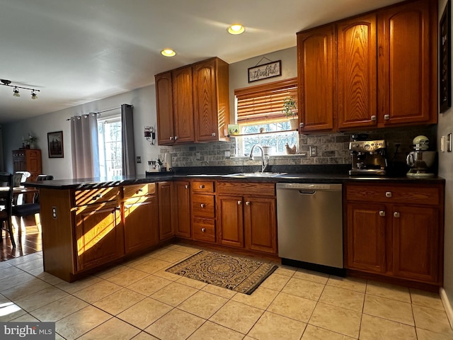 kitchen with dark countertops, dishwasher, decorative backsplash, a peninsula, and a sink