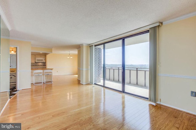 unfurnished living room featuring light wood finished floors, floor to ceiling windows, a textured ceiling, and ornamental molding