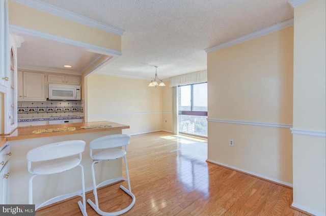 kitchen with white microwave, crown molding, light wood-style flooring, a peninsula, and a textured ceiling