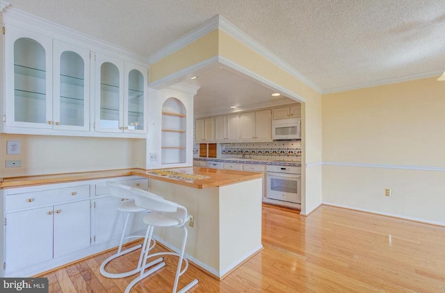 kitchen with white appliances, ornamental molding, light countertops, light wood-style floors, and a textured ceiling