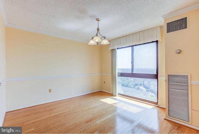 spare room with visible vents, an inviting chandelier, wood finished floors, and crown molding