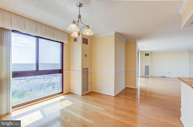 empty room with an inviting chandelier, plenty of natural light, visible vents, and light wood finished floors