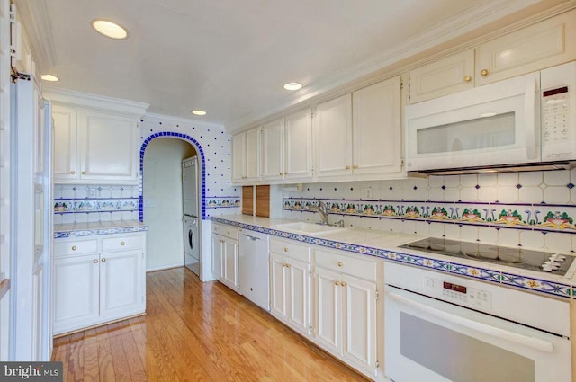 kitchen featuring light wood finished floors, light countertops, stacked washer and clothes dryer, white appliances, and a sink