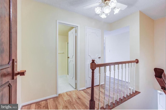 hall featuring an upstairs landing, a textured ceiling, light wood-type flooring, and baseboards