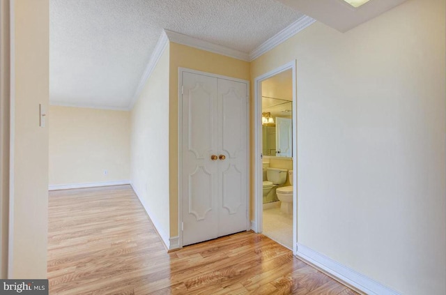 hall featuring a textured ceiling, crown molding, baseboards, and wood finished floors