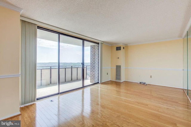 spare room featuring wood finished floors, visible vents, floor to ceiling windows, a textured ceiling, and crown molding