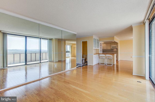 unfurnished living room with light wood-type flooring, a textured ceiling, and crown molding