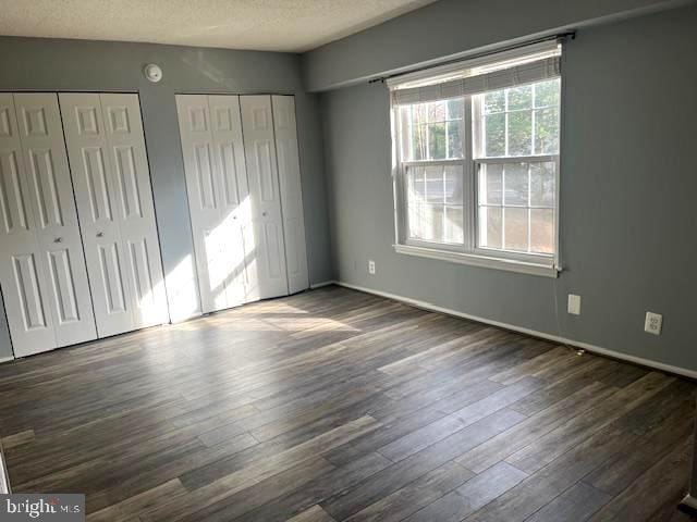 unfurnished bedroom featuring a textured ceiling, multiple closets, and dark wood-style flooring