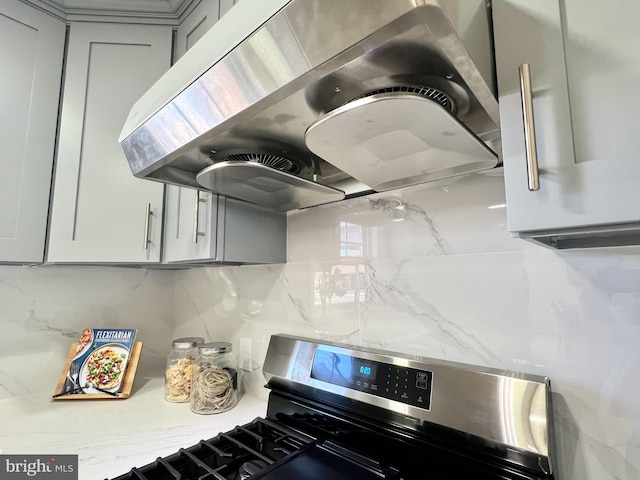 kitchen with stainless steel gas range oven, gray cabinetry, light stone counters, exhaust hood, and decorative backsplash