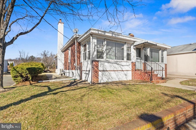 view of front of house featuring brick siding, a chimney, a front yard, and a sunroom