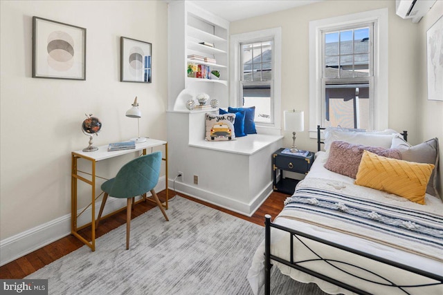 bedroom featuring baseboards, a wall unit AC, and wood finished floors