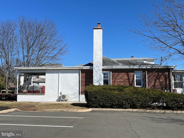 view of front of home featuring stucco siding, uncovered parking, brick siding, and a chimney