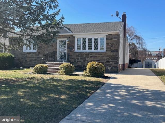 view of front of property with a front yard, a chimney, concrete driveway, an outdoor structure, and stone siding