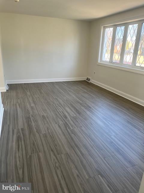 unfurnished room with dark wood-style floors, visible vents, and baseboards