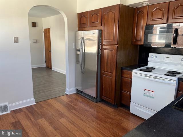 kitchen featuring visible vents, electric stove, dark wood-style floors, arched walkways, and stainless steel fridge with ice dispenser