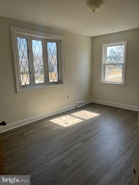 empty room with visible vents, baseboards, and dark wood-style flooring