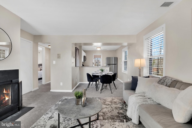 carpeted living area featuring visible vents, a fireplace with flush hearth, and baseboards