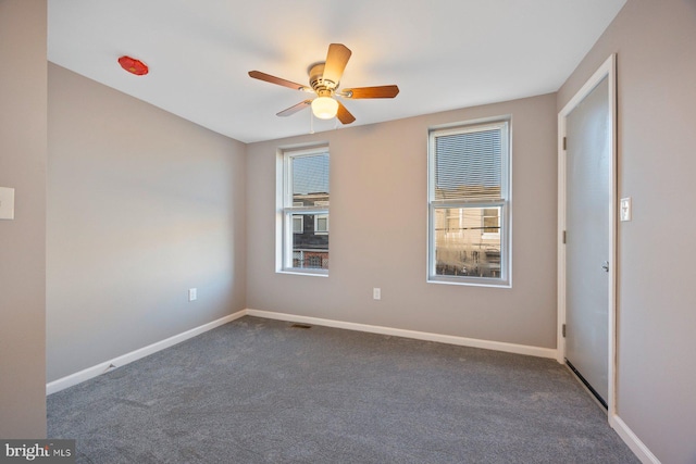 empty room featuring dark colored carpet, visible vents, baseboards, and a ceiling fan