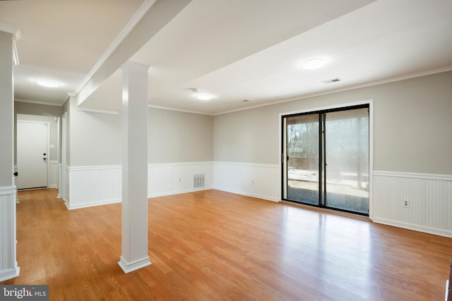 empty room featuring visible vents, wainscoting, crown molding, and light wood-type flooring