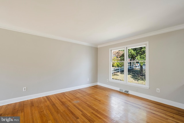 empty room with light wood-type flooring, visible vents, baseboards, and crown molding