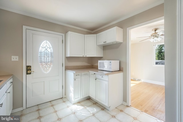 kitchen with white microwave, visible vents, light countertops, ornamental molding, and white cabinetry