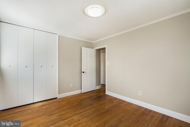 unfurnished bedroom featuring a closet, ornamental molding, baseboards, and hardwood / wood-style flooring