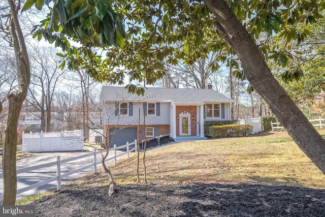 split foyer home featuring concrete driveway, fence, brick siding, and a chimney