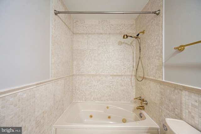 full bath with toilet, tile walls, and a combined bath / shower with jetted tub