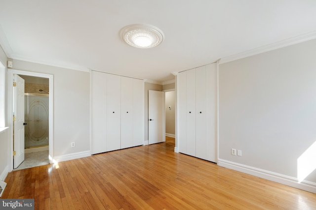 unfurnished bedroom featuring light wood-style flooring, baseboards, multiple closets, and ornamental molding