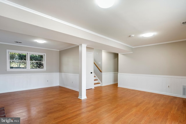 basement featuring a wainscoted wall, light wood finished floors, ornamental molding, and stairway