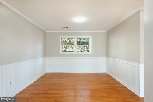 spare room featuring light wood-type flooring, visible vents, and a wainscoted wall