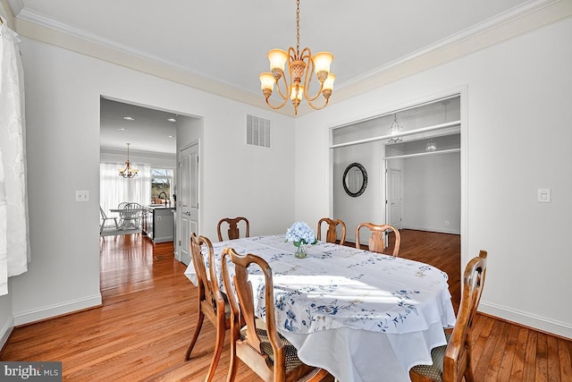 dining space featuring an inviting chandelier, crown molding, visible vents, and light wood-type flooring