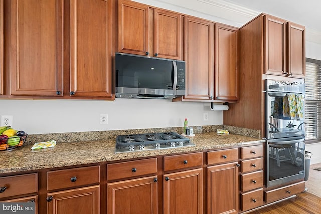 kitchen featuring wood finished floors, light stone counters, brown cabinetry, and appliances with stainless steel finishes