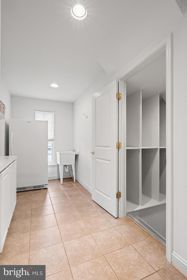 hall featuring light tile patterned floors, baseboards, and a sink