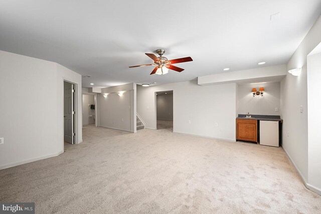 unfurnished living room with stairway, a ceiling fan, baseboards, indoor wet bar, and light carpet