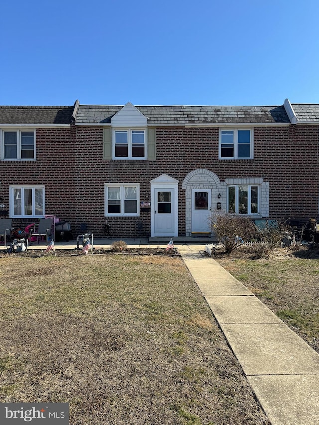 view of property featuring a patio, brick siding, and a front lawn