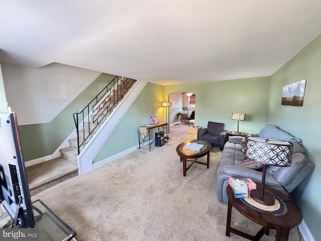 carpeted living area with arched walkways, stairway, and baseboards