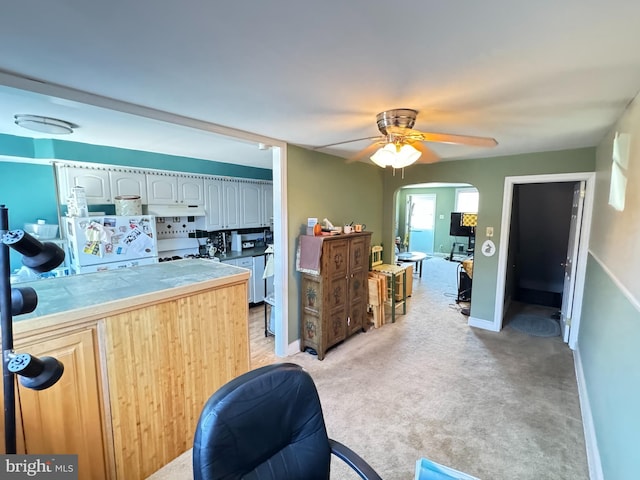 kitchen with under cabinet range hood, freestanding refrigerator, tile countertops, arched walkways, and light colored carpet