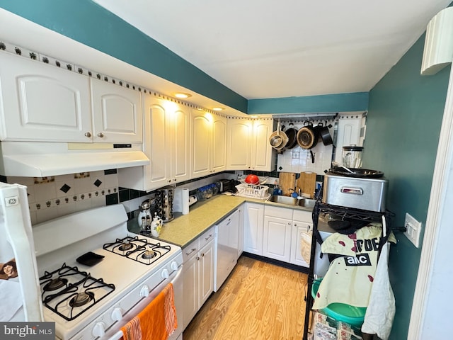 kitchen featuring white appliances, light wood finished floors, a sink, decorative backsplash, and under cabinet range hood