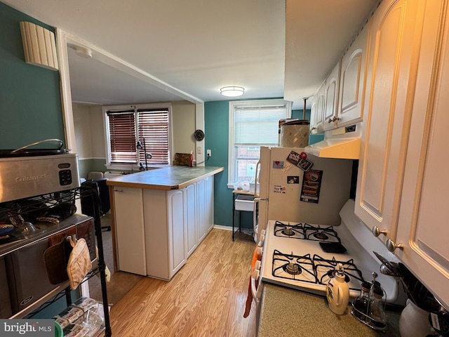 kitchen with light wood-type flooring, range hood, a peninsula, white cabinets, and white appliances