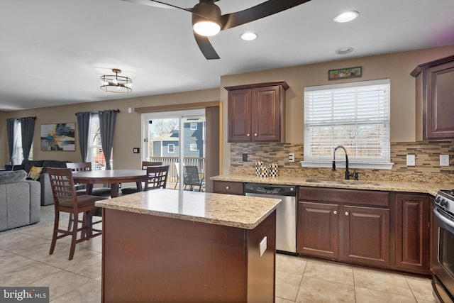 kitchen with light stone counters, a kitchen island, ceiling fan, a sink, and stainless steel dishwasher