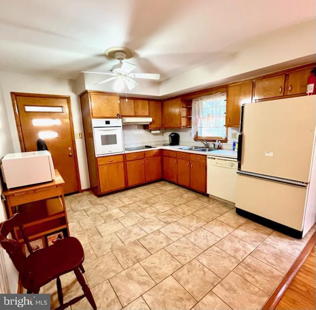 kitchen with white appliances, a sink, light countertops, under cabinet range hood, and brown cabinets