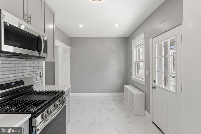 kitchen with marble finish floor, backsplash, stainless steel appliances, light countertops, and baseboards