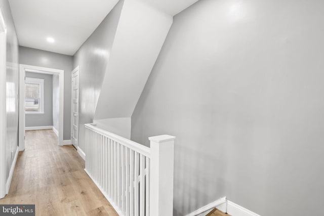 hall featuring an upstairs landing, baseboards, and light wood finished floors